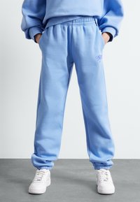 Pantalones de chándal azul claro, confeccionados en una tela suave, con una cinturilla y puños elásticos, y un sutil bordado de la marca en la parte frontal.