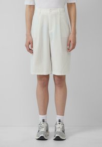 Witte gestreepte shorts met een hoge taille en plooien, voorzien van een knoopsluiting aan de voorkant. Gecombineerd met zilveren sportschoenen en witte sokken.