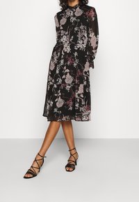 Black floral dress with long sleeves and button closure, featuring a delicate pattern of pink and gray flowers, paired with black strappy sandals.