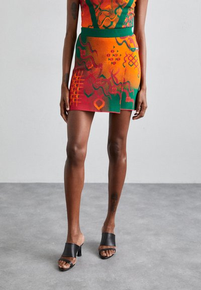 Farverig nederdel med en blanding af orange, grønne og røde mønstre med geometriske designs. Matcher med sorte åbne mules med hæl.