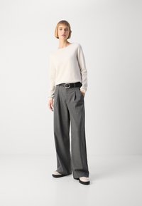 Light beige sweater with long sleeves, paired with gray pleated wide-leg trousers and black belt featuring a round silver buckle. Footwear with light accents.