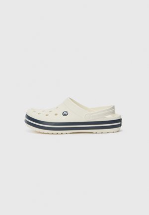 Hvide slip-on træsko med perforeret tåområde og navyblå dobbelte striber omkring sålen, med justerbar rem ved hælen.