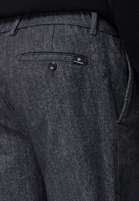 Ciemnoszare spodnie w jodełkę, z pojedynczą tylnią kieszenią zapinaną na guzik oraz metką marki. Gładka tekstura.