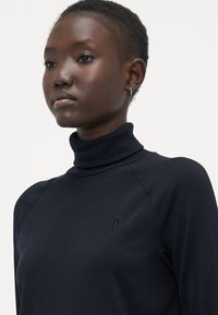 Granatowy sweter typu golf wykonanego z gładkiego, elastycznego materiału. Posiada dopasowany fason i subtelny detal z logo na klatce piersiowej.