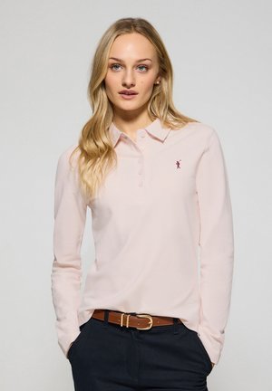 Langsleeve polo shirt van zacht roze stof, met een button-up kraag en een klein rood embleem op de linkerborst. Gekoord met een bruine riem.