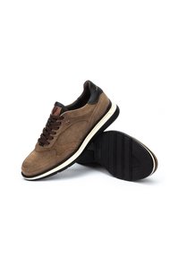 Zapatillas de ante marrón con acentos en negro, punta redonda y suela con patrón. Presentan cordones marrones y un logo decorativo en la lengüeta.