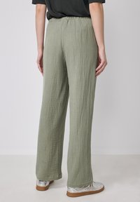 Light olive green wide-leg pants made of textured fabric, featuring an elastic waistband and falling to the ankles, paired with silver shoes.