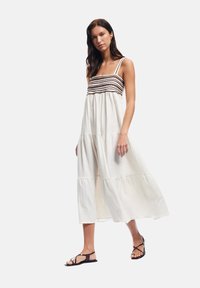 Maxikleid in Creme mit einem strukturierten Stoff und einem Zickzackmuster in Braun über der Brust; hat dünne Träger und einen lässigen Schnitt.