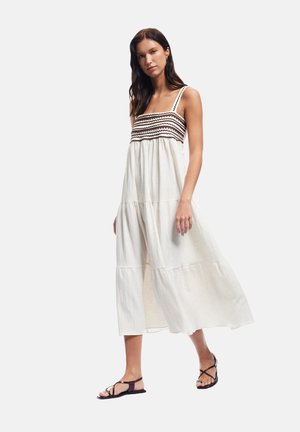 Abito maxi color crema in tessuto testurizzato con un motivo a zigzag marrone sul decolletè; presenta spalline sottili e vestibilità comoda.