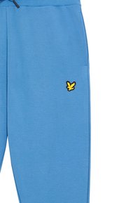 Blauwe joggingbroek met elastische taille, voorzien van een gele en zwarte geborduurde logo aan de linkerkant en zijzakken. Soepele textuur.