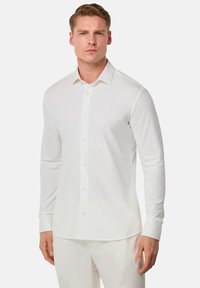 Camicia bianca a maniche lunghe con bottoni, realizzata in tessuto liscio, caratterizzata da un colletto classico, taglio dritto e semplici dettagli con bottoni.