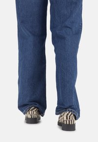 Jean en denim avec une finition bleu délavé et des jambes droites, associés à des chaussures texturées à motifs noir et blanc avec une semelle épaisse.