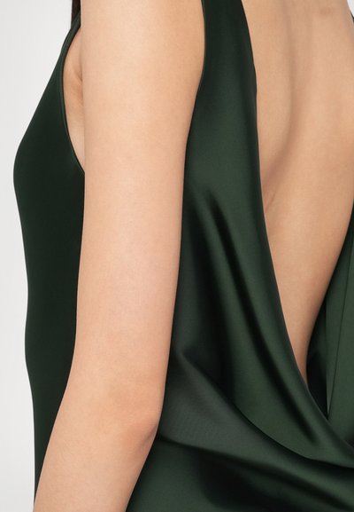 Ciemnozielona sukienka bez rękawów z głębokim wycięciem na plecach. Materiał jest gładki i błyszczący, z delikatnym drapowaniem po boku.