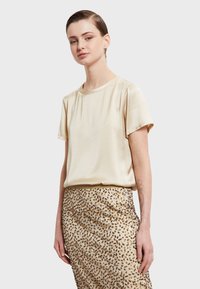 Krátky rukáv, krémové saténové tričko s okrúhlym výstrihom. Skombinované so sukňou s textúrou a zlatými bodkami, ktorá ponúka hladký a lesklý vzhľad.