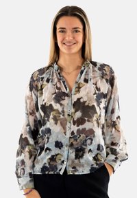 Blusa floral ligera y transparente con tonos de azul, marrón y crema, con cierre de botones, mangas largas y un corte relajado.