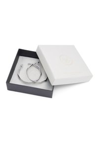 Pendientes de aro plateados con un diseño retorcido, acomodados en un suave forro interior blanco, dentro de una caja negra con una tapa texturizada blanca.
