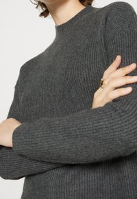 Dunkelgrauer gerippter Pullover mit hohem Kragen und langen Ärmeln, aus einem weichen Stoff mit strukturierter Oberfläche gefertigt.