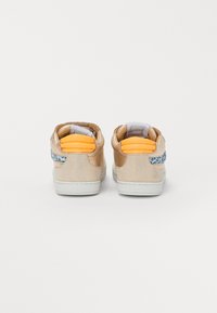 Baskets en cuir beige avec une finition texturée, accents de talon orange et bord bleu avec un motif sur le côté. Semelle en caoutchouc blanche.
