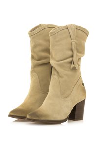 Botas de tobillo de ante beige con un diseño ligeramente holgado, punta afilada y tacón apilado. Presenta borlas decorativas y detalles de costura.
