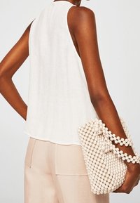 Top blanco sin mangas con un acabado texturizado, combinado con un bolso beige adornado con cuentas redondas, que presenta un diseño de tirantes fruncidos.