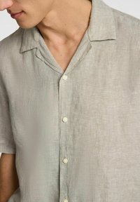 Jasnoszara, krótko rękawowa koszula lniana z kołnierzykiem i przednimi guzikami. Tekstura wydaje się nieco pognieciona, ale ma gładkie wykończenie.