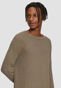 Pull en maille de couleur vert olive, avec un motif texturé et un col rond. Des manches longues et une coupe décontractée complètent le design.
