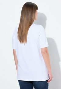 T-shirt blanc à manches courtes en coton doux, avec une coupe décontractée et un col rond, porté avec un jean bleu marine.