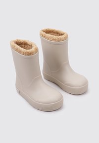 Botas impermeables beige con un suave forro de piel sintética color marrón y suelas de goma texturizada para mayor agarre. Altura a medio pantorrilla con una superficie lisa.