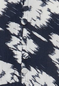 Modrý a bílý vzorovaný textil s designem vlny, se šesti kulatými knoflíky umístěnými svisle podél předního zapínání.