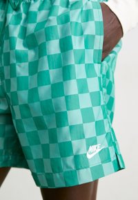 Turkise rutete shorts laget av lett materiale, med sidelommer og en hvit Nike-logo på den nedre sømmen.