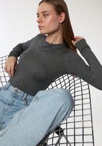 Szary sweter z długim rękawem, okrągłym dekoltem, w połączeniu z jasnoniebieskimi spodniami z wysokim stanem, siedzący na krześle w kształcie siatki.