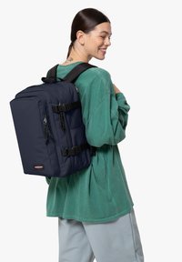Zaino navy realizzato in tessuto resistente, dotato di due tasche frontali, spallacci regolabili e accessori neri. Indossato sulla schiena di una persona.