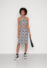 Conjunto de top cropped e saia com padrão em preto e branco, apresentando um decote halter e cintura com cordão; combinado com ténis altos pretos e uma bolsa preta.