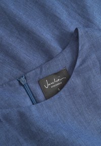 Tume sinine linane kangas ümmarguse kaelusega, millel on tõmblukk ja silt, millel on kirjas "Jascha Stockholm S" suuruse tuvastamiseks.