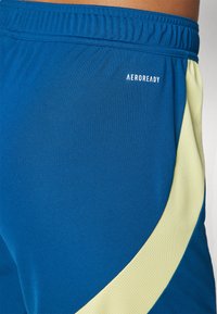 Mėlyni sportiniai šortai su geltonu tinkliniu akcentu. Yra patogus elastingas juosmuo ir balta AEROREADY logo. Lygus paviršius.