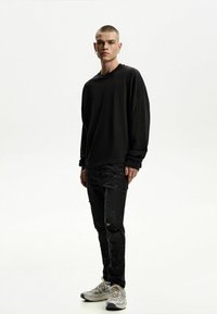 Cămașă neagră oversized cu mâneci lungi, blugi negri distruși cu stropi de vopsea și adidași gri cu accente bej.