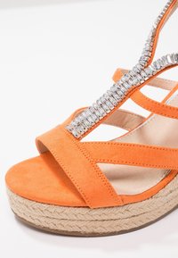 Sandale compensée en daim orange avec plateforme en jute tressée et bride en T ornée de cristaux sur semelle intérieure beige.