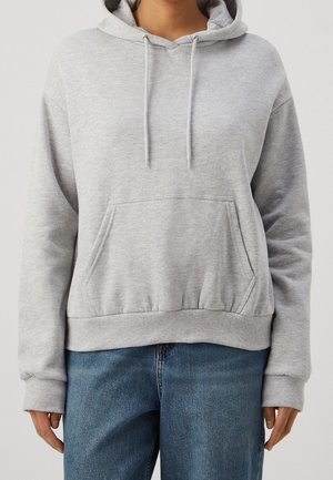 Person trägt ein hellgraues Kapuzen-Sweatshirt mit Fronttasche und Kordelzug, kombiniert mit blauen Jeans aus Denim.