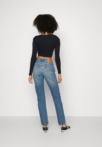 Jeans de mezclilla de color azul claro con un corte recto, bolsillos traseros y un parche de cuero marrón. Combinados con una camiseta negra de manga larga corta y zapatillas negras.
