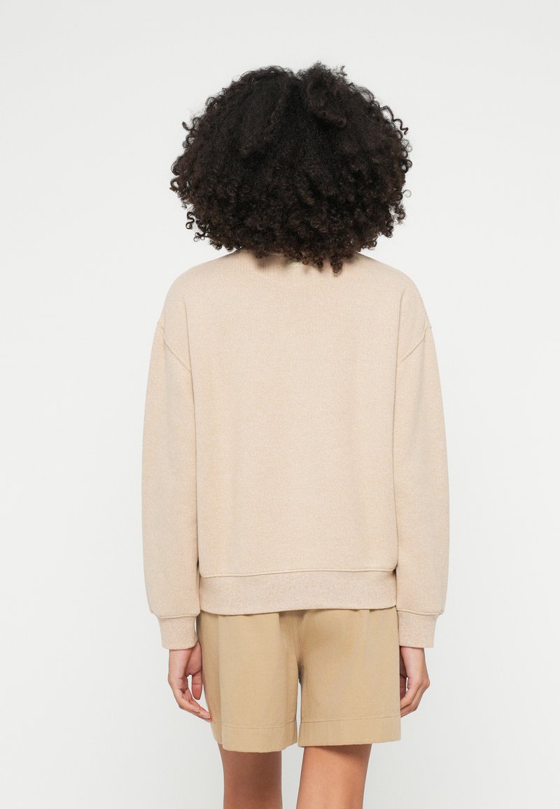 Beige sweatshirt met een ontspannen pasvorm, geribde manchetten en zoom. Gecombineerd met bruine shorts, de stof is zacht met een subtiele textuur.