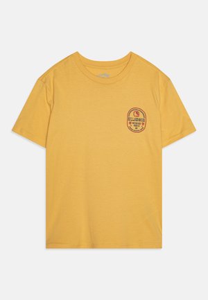 T-shirt en coton jaune à manches courtes, col rond, avec un patch circulaire rouge et noir sur la partie gauche de la poitrine.