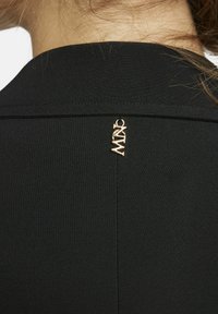 Zwarte kledingstuk met een gestroomlijnd ontwerp en een gladde textuur, met een gouden hardware accent in de vorm van de merknaam op de achterkant.