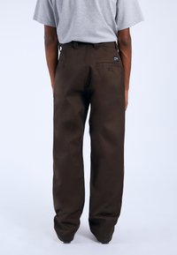 Braune, gerade geschnittene Hosen aus robustem Stoff, mit einer Gesä�ßtasche und einem kleinen Logotag. Der Schnitt ist locker und minimalistisch.