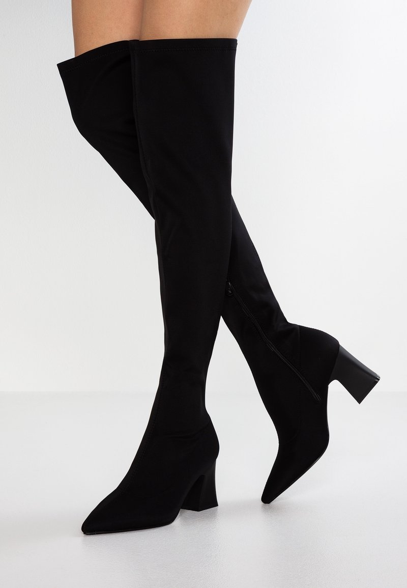 Bottes noires hautes en latex, dotées d'un bout pointu et d'un talon carré, avec une fermeture à glissière sur le côté.