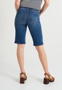 Bermudas en denim bleu foncé, longueur genou avec ourlets repliés, comportant deux poches arrière et une taille mi-haute.