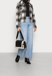 Svart och vit rutig jacka, höghalsad svart topp, ljus tvätt med vida jeans och svarta klackboots, bär en svart och beige handväska.