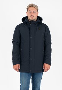 Parka isolata blu navy con cappuccio, bottoni frontali, due tasche laterali e un morbido rivestimento interno. Progettata per calore e protezione.