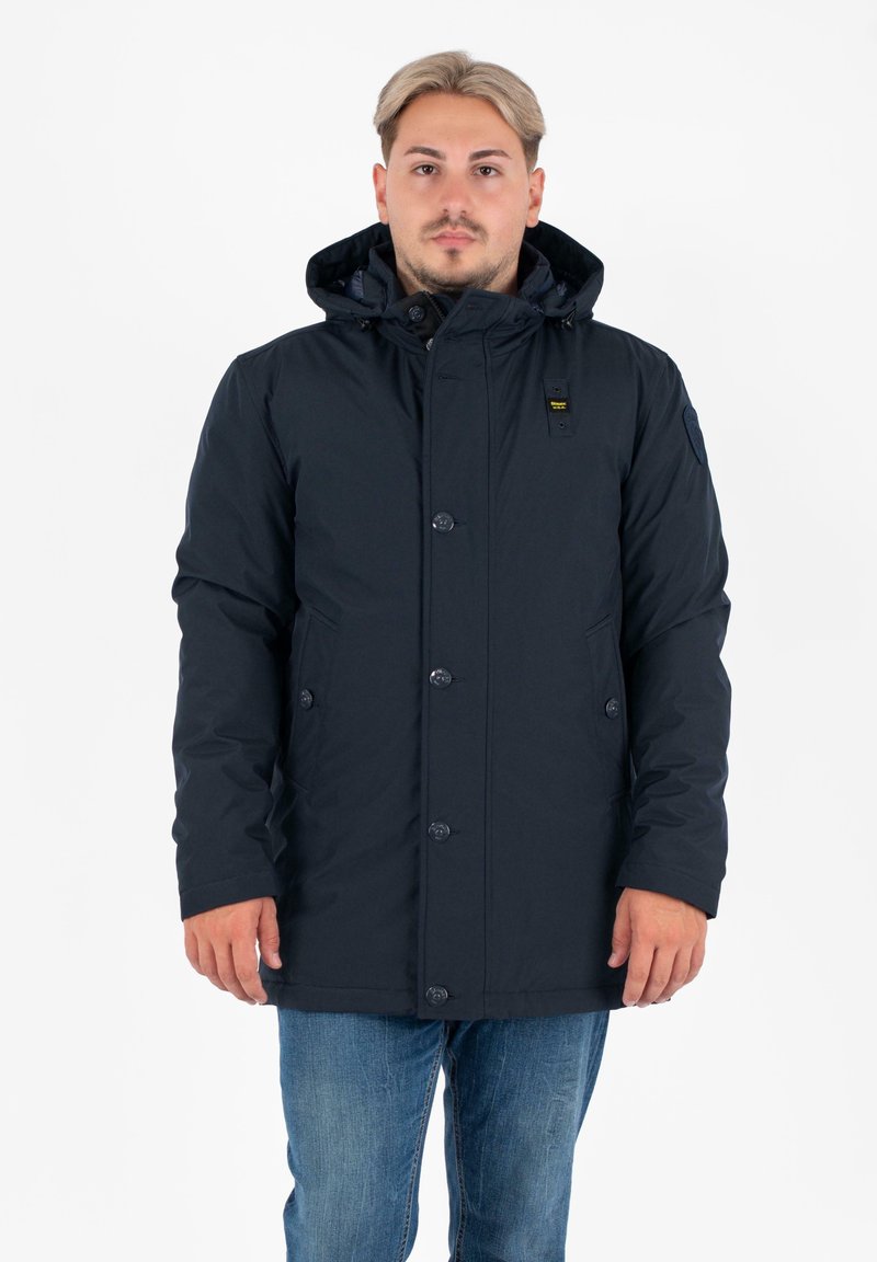 Parka isolata blu navy con cappuccio, bottoni frontali, due tasche laterali e un morbido rivestimento interno. Progettata per calore e protezione.