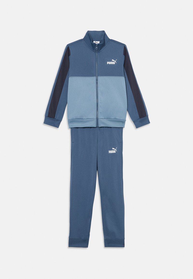 Dwuczęściowy dres w kolorze niebieskim z kontrastującymi ciemnoniebieskimi rękawami. Zawiera zapinana na zamek kurtkę oraz zwężane spodnie z małym logo na obu elementach.