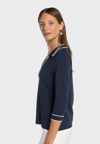 Pull-over bleu marine avec un col défini, des accents rayés blancs, des manches trois-quarts et une coupe décontractée. Texture en tricot doux.